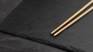 the tips of two cream coloured chopsticks, against a dark grey placemat
