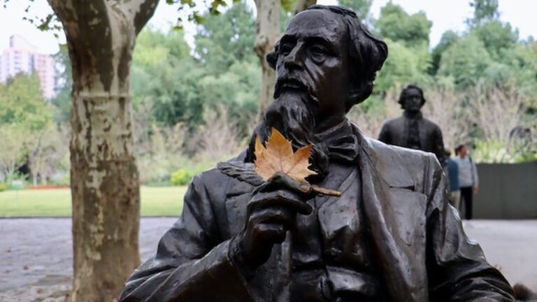 A statue of Charles Dickens, holding a pen, with a fallen leaf resting on his neck