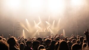 multiple spotlights pour onto a stage before the head and arms of an audience