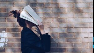 a woman holds a book right against her head so she can't read it