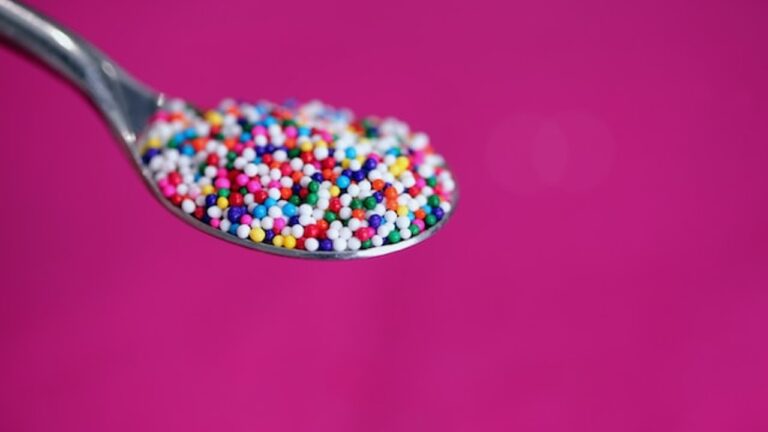 a teaspoon containing hundreds of tiny multicoloured granules, set against a purple background