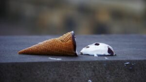 an ice cream cone lying flat with the ice cream itself lying at a short distance having been spilt