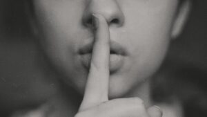 a close up of a woman with a finger to her mouth, gesturing silence