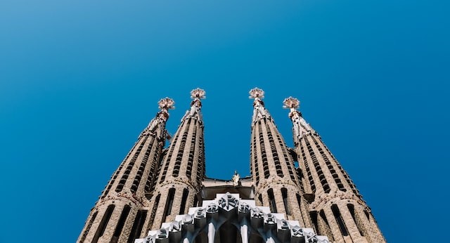 A view looking up at four of the spires of the Sagrada Familia cathedral, against a blue sky