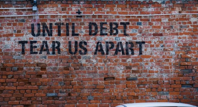 a brick wall with stencilled graffiti saying "Until debt tears us apart"