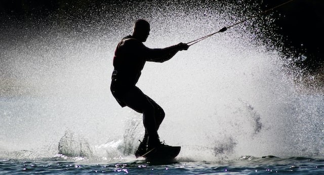 a silhouette photo of a waterskier, seen in profile, kicking up spray