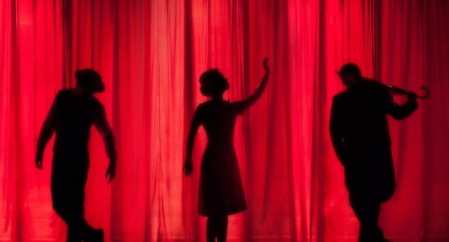 a silhouette of three cabaret performers posing against a lush red curtain