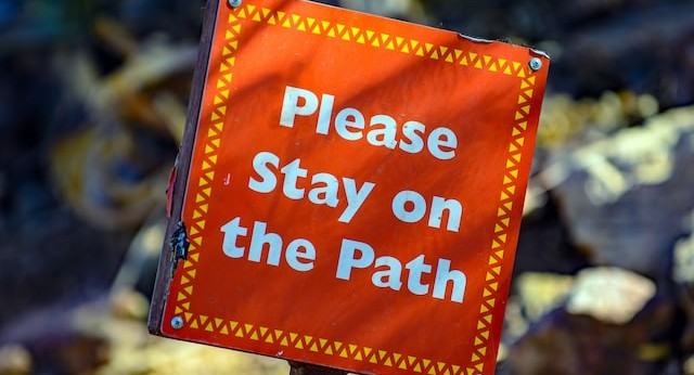 An orange sign saying "Stay on the path"