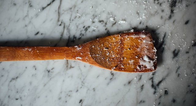 a wooden spatula with crumbs of raw dough on it, against a marble backdrop