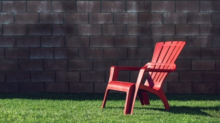 a bright red lawn chair, on a green lawn against a dark wall in the background