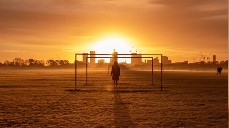 a silhouette of a person standing between goal posts, set against a sunset
